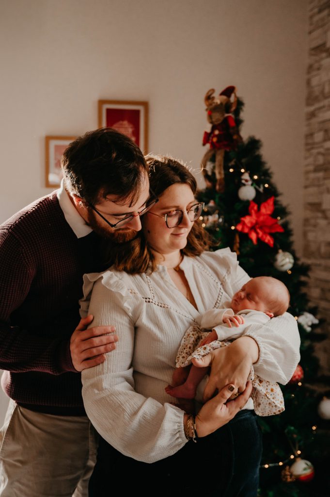 Nouveau né dans les bras de ses parents à Noël devant le sapin 